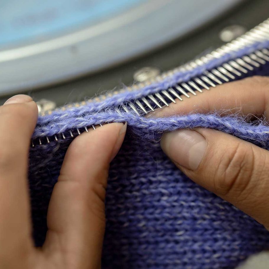 Verarbeitung der Wolle - Die Geschichte der Alpakawolle Hände, die an einem lila Alpaka Wolle mit einer Strickmaschine arbeiten.