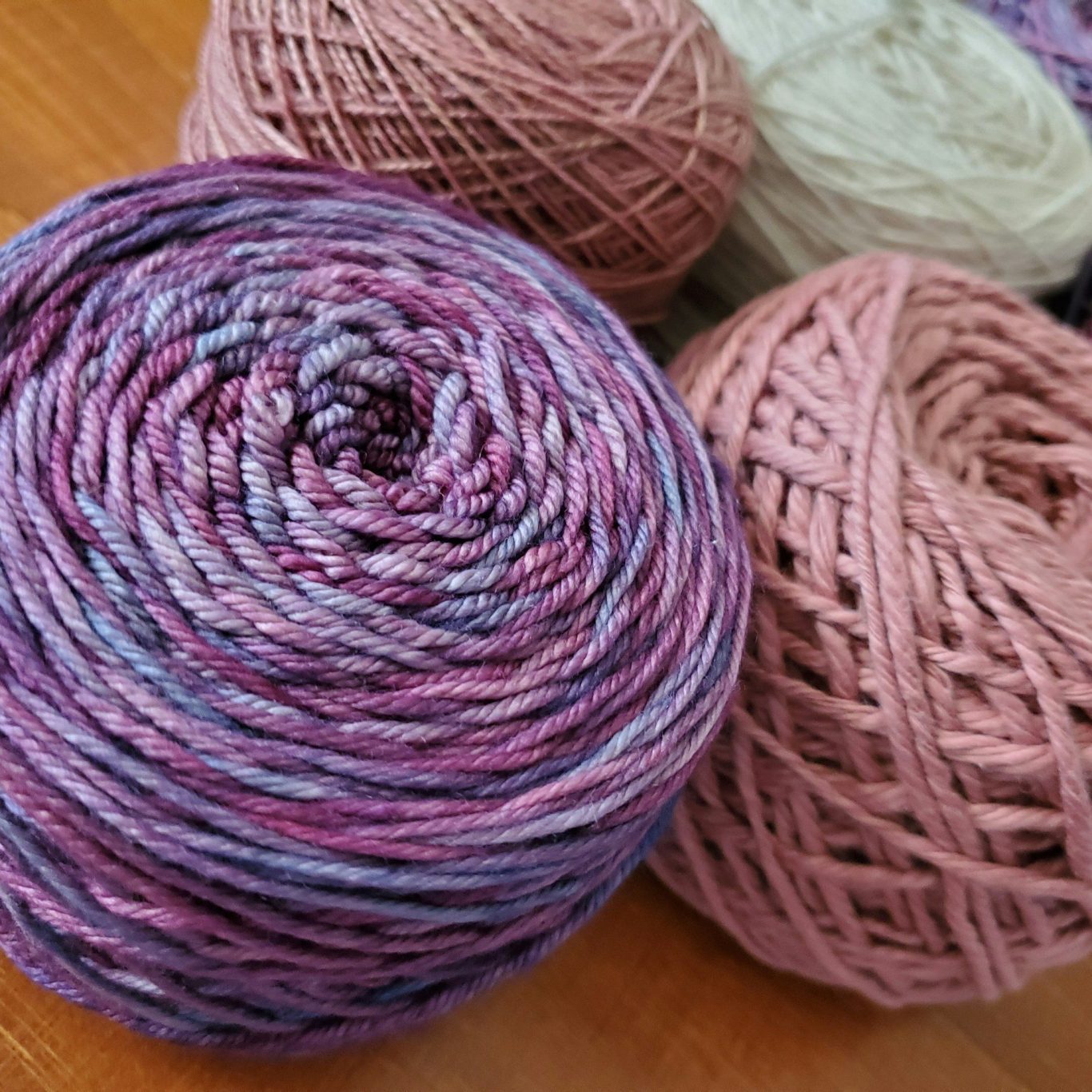Merino Wolle - Alpaka oder Merino – Die wichtigsten Unterschiede Bunte Merino Garnknäuel in verschiedenen Rosa- und lila Farbtönen auf einem Tisch.