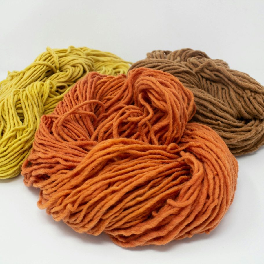 Merino Wolle - Alpaka oder Merino – Die wichtigsten Unterschiede Drei Knäuel Merino-Wolle in den Farben Gelb, Orange und Braun auf weißem Hintergrund.